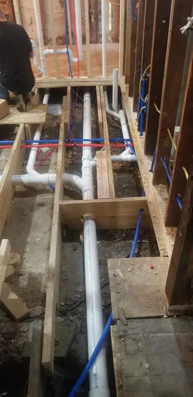 New plumbing rough-in with PVC drain lines and PEX supply lines in an open wall