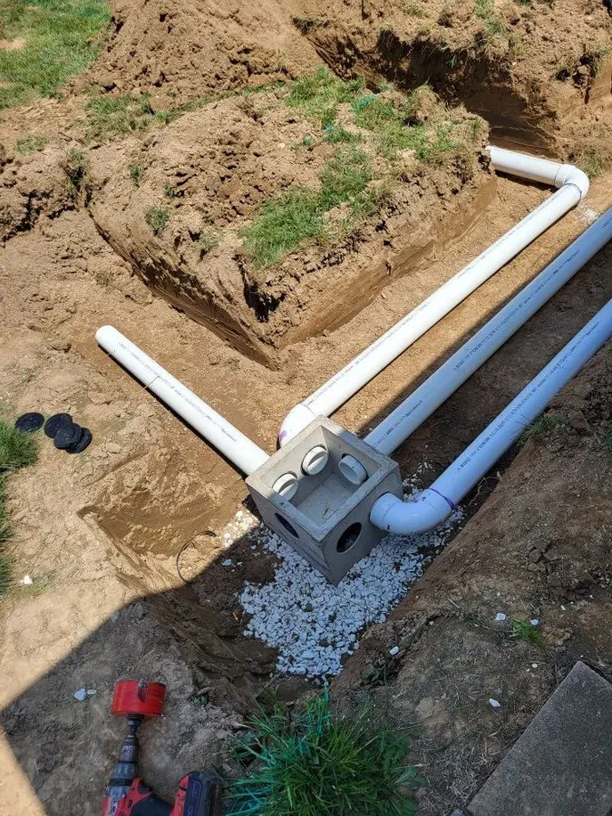 Excavated yard showing a new PVC drain line and cleanout installed by Elite